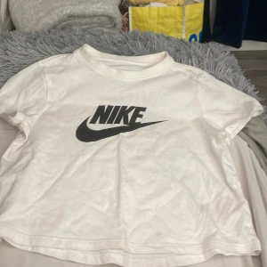 Vit Nike t-shirt med logga - Vit t-shirt från Nike med klassisk svart logga framtill. Modellen är kortärmad och har en avslappnad passform. Perfekt för dig som gillar sportiga och stilrena plagg. Tillverkad i mjuk bomull för skön känsla hela dagen.