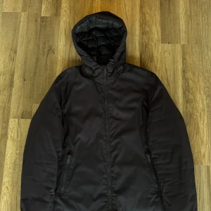 Svart pufferjacka från Massimo Dutti - Svart pufferjacka från Massimo Dutti med huva och dragkedja. Jackan är lätt, vindtät och vattenavvisande. Quiltad insida och praktiska fickor med dragkedja. Perfekt för kyliga dagar när du vill hålla stilen och värmen.