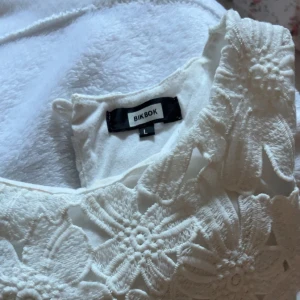 Vit blommig ärmlös topp från Bik Bok - Superfin vit ärmlös topp från Bik Bok med stora broderade blommor över hela tyget. Toppen har en rak passform och är fodrad under det blommiga spetslagret. Perfekt att styla med jeans eller kjol för en fräsch look. Den är i storlek L men skulle säga M/S då den passar mig som vanligtvis bär S