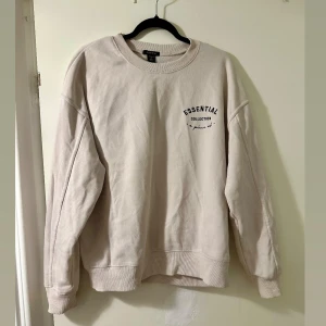 Beige Essential sweatshirt  - Säljer en beige sweatshirt från Asher Essential Collection med svart tryck på bröstet. Tröjan har rund halsringning, långa ärmar och ribbade muddar. Perfekt för en chill och avslappnad stil.