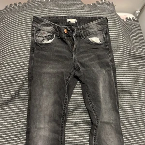 Svarta jeans från Gina Tricot, stl 158 - Snygga svarta jeans från Gina Tricot i storlek 158. Jeansen har en tvättad look, dragkedja och knapp framtill samt coola bakfickor med broderade detaljer. Klassisk femficksmodell och bälteshällor. Perfekta till en avslappnad stil. Low waist.