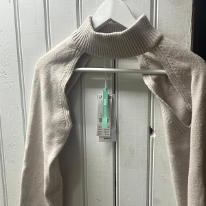 Beige stickad polotröja från Gina Tricot - Trendig beige stickad polotröja från Gina Tricot med ribbad hög krage och lång ärm, är i mjukt material.