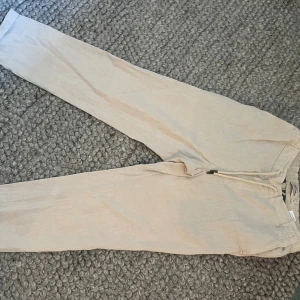 Beiga linnebyxor från Dressmann XS - Snygga beiga linnebyxor från Dressmann i storlek XS. Byxorna har dragsko i midjan för skön passform och är tillverkade i en luftig linneblandning. Perfekta för varmare dagar när du vill ha en avslappnad men stilren look.