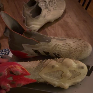 Adidas Predator Demonskin fotbollsskor - Säljer ett par Adidas Predator elite Demonskin fotbollsskor i grått med svarta detaljer och röda inslag vid hälen. Skorna har en högre strumpliknande krage och taggig ovansida för extra grepp på bollen. Snygg och modern design, perfekta för dig som vill sticka ut på planen. Priset är inte hugget i sten 