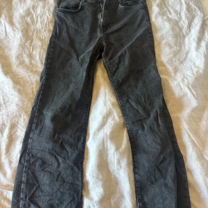 Svarta jeansbyxor från Zara, strl 38 - Snygga svarta jeansbyxor från Zara i storlek 38. Klassisk femficksmodell med raka ben och normal passform. Jeansen har en mörk tvätt och är tillverkade i mjukt denim-material med knapp och dragkedja framtill.