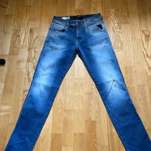 Replay Anbass Hyperflex jeans blå - Snygga Replay Anbass Hyperflex jeans i mellanblå tvätt med lätt slitning och klassisk femficksdesign. Jeansen har normal passform och är tillverkade i stretchigt jeansmaterial för extra komfort. Perfekta för dig som gillar stilrena och bekväma jeans.