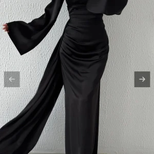 Lång satinklänning med vida ärmar - Säljer en elegant långklänning i satin med markerad midja, draperad detalj och vida ärmar. Klänningen har en slits på sidan och finns i svart, marinblå och ljus mintgrön. Perfekt för dig som vill sticka ut med en stilren och lyxig look.