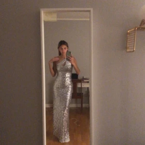 Silvrig glittrig balklänning - Säljer denna fina silverglittriga klänning som är perfekt till bal eller liknande ! Är i princip som ny och knappt använd. Den har små silvriga paljetter och öppen rygg som man kan se på bilden. Kommer från nly eve i strl 34. Hör av er vid frågor💗