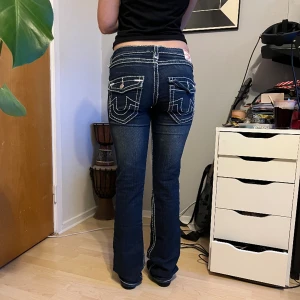 True Religon Jeans - True Religon jeans som är raka i benen/ lite utsvängda vid anklarna, mörka med vit sömn ( saknas en knapp på ena fickan men inget märkbart ❤️)  -midjemått rakt över = 42 cm -innerbenslängd = 84 cm -längd på hela= 106 cm