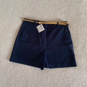ZARA marinblåa shorts med guldigt skärp - Kostymshorts med hög midja från ZARA i marinblå färg med ett tunt guldigt skärp. Aldrig använda, nya med tags och utan anmärkningar.