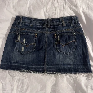 Jeanskjol med nitar - Cool jeanskjol i fin färg med massa detaljer, midjemått rakt över: 40cm, längd: 32cm. Kolla gärna in våra andra annonser!