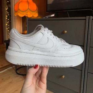 Nike Court Vision Alta - Nike Court Vision Alta i storlek 37,5. Väl omhändertagna, insmorda ofta med vit skokräm för att bevara färg och läder. Skosnören byta en gång. Defekten som finns är små hål i hälarna, se bilder. Annars fina och hela.