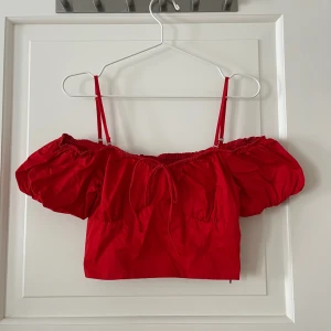 Topp från Zara - Off-shoulder blus i röd från Zara. Volangärm med band som är avtagbara. Storlek M och passar S-M. Markerad vid bysten och rosett framtill. Stängs med dragkedja på sidan. Rynkad baksida men rynkingen har ”dragits upp” på två ställen. Finns fler bilder