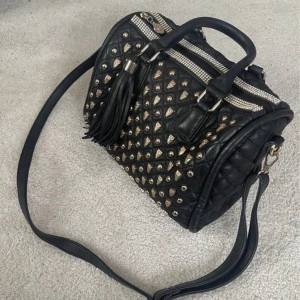 Handväska - Jättefin secondhand väska med gulddetaljer. Är i väldigt bra skick och har hantag och en större.