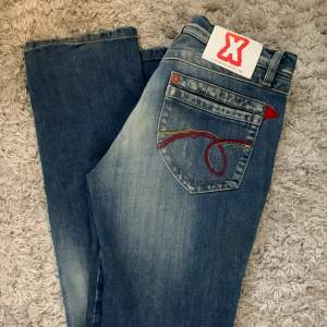 Lågmidjade unika jeans med röda detaljer. Vet ej stl men de är 38 cm rakt över midjan och innerbenslängden är 85 cm. Knappt använda