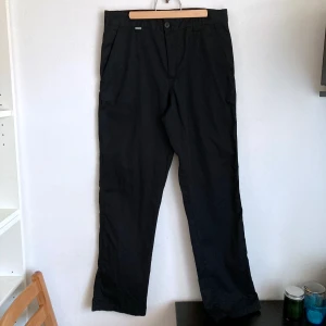 Svarta arbetsbyxor, 46 S, straight leg, regular waist - Svarta raka arbetsbyxor, två sidfickor, två bakfickor, 65% polyester & 35% bomull. Finns några noppor samt lätt urtvättade. Mått i cm: midja 39; höft 50; benvidd nedanför grenen 30; benöppning 19; grenhöjd fram/bak 26/37; innerben 78.