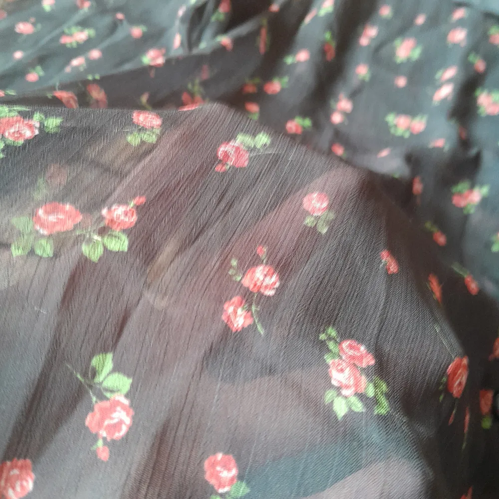 En svart blus med små röda blommor, i semi-transparent mesh tyg. Knappar fram och väldigt söt veckad krage. Storlek L, men sitter bra, lite oversize, på mig som vanligtvis har S/M. Helt ny, har inte blivit av att jag använt tyvärr.. Puserot.