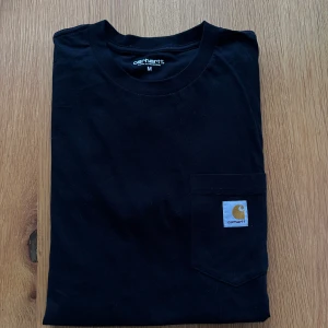 Svart T-shirt  - Oanvänd T-shirt från Carhartt. Finns även i vit, se min profil.  Rensar ur min garderob från en hel del oanvända kläder🌼 Om du ser något mer i min profil som du gillar så skickar jag med det till dig också!😊 Fler kläder kommer!