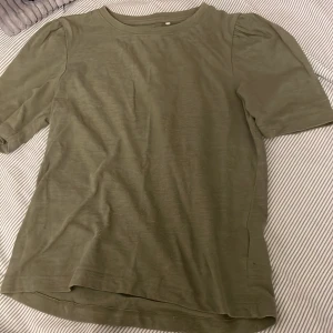 Olivgrön topp - En olivgrön topp med korta ärmar och rund halsringning. Toppen har en enkel design och är tillverkad i ett mjukt material.