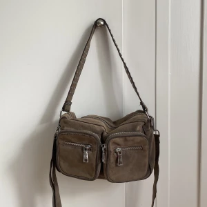 Axelremsväska  - Super snygg och användbar väska från Noella. Nästan helt oanvänd och har en väldigt praktisk färg som tål slit och smuts. 