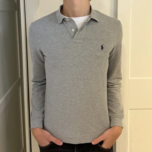 Långärmad Ralph Lauren piké  - Långärmad Ralph Lauren piké i färgen grå. Inga defekter på tröjan. Size S (slim fit) modellen är 177cm. Hör av dig vid funderingar!