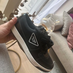 Svarta sneakers från Prada - Ett par svarta sneakers från Prada med vit sula och svart snörning.  str 42 jag har änvend bara 2 gånger det finns box också 