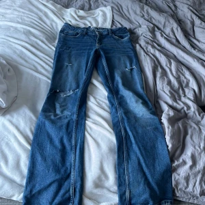 Low Waist bootcut jeans - Low waist bootcut jeans från Gina tricot young size. Byxorna är använda men inte slitna. Hålen är klippta för att få jeansen unika. Det går även att spänna åt jeansen i midjan