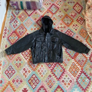 Originell läderjacka med avtagbar luva och vita sömmar - Läderjacka storlek L/XL. Vita sömmar, avtagbar luva. Bra skick, förutom litet hål (se bild)