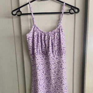 Oanvänd Blommig lila klänning storlek Xs - Jag säljer denna helt nya blommiga sommarklänningen i storlek xs. Den går till knäna och sitter fint. Säljer pågrund av att den tyvärr inte använts.