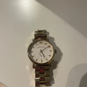 Klocka från Marc Jacobs  - Klocka i guld från Marc Jacobs. Klockan har några repor på uret och saknar fungerande batteri. Armbandet går att ställa in. I övrigt bra skick! 