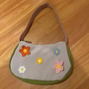 Blommig beige väska med gröna och rosa detaljer.