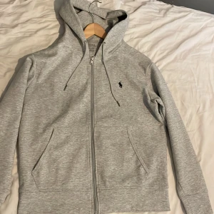 Polo Ralph lauren zip hoodie  - En grå Ralph lauren zip hoodie i storlek S men passar även M. Fick den i julklapp men den var lite för liten för mig. Den är använd ett fåtal gånger och är fortfarande i väldigt bra skick.