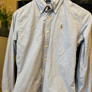 Ralph Lauren skjorta dam  - Fin Ralph Lauren skjorta i ljusblå färg för dam med sytt märke. Sparsamt använd. Storlek 6 och slimfit modell vilket motsvara ungefär S. 