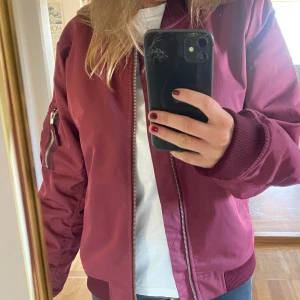 Vinröd bomberjacka  - Så snygg bomberjacka i nyskick! Storlek L men känns mer som en M, jag är ca 1.63 lång 