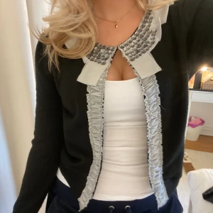Tunn kofta  - Säljer denna svarta kofta, med diamanter och volanger vid kragen. Jättesöt passform! Har älskat den men använder inte längre💗
