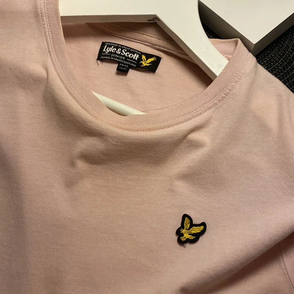 Ljusrosa t-shorts ifrån lyle and Scott, färgen blir inte rättvis på bild men är i fin ljusrosa nyans🫶🏼💞 är i storlek 14/15 år men passar mig som har S . T-paidat.