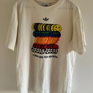 T-shirt med tryck från Adidas - Tröja från Adidas med snyggt tryck fram. Köpt på second-hand butik och är i väldigt fint skick! Passar mig bra som är 188. Skulle säga att den sitter som en M. Riktigt fräsch inför sommaren! Hör av dig vid minsta fundering!