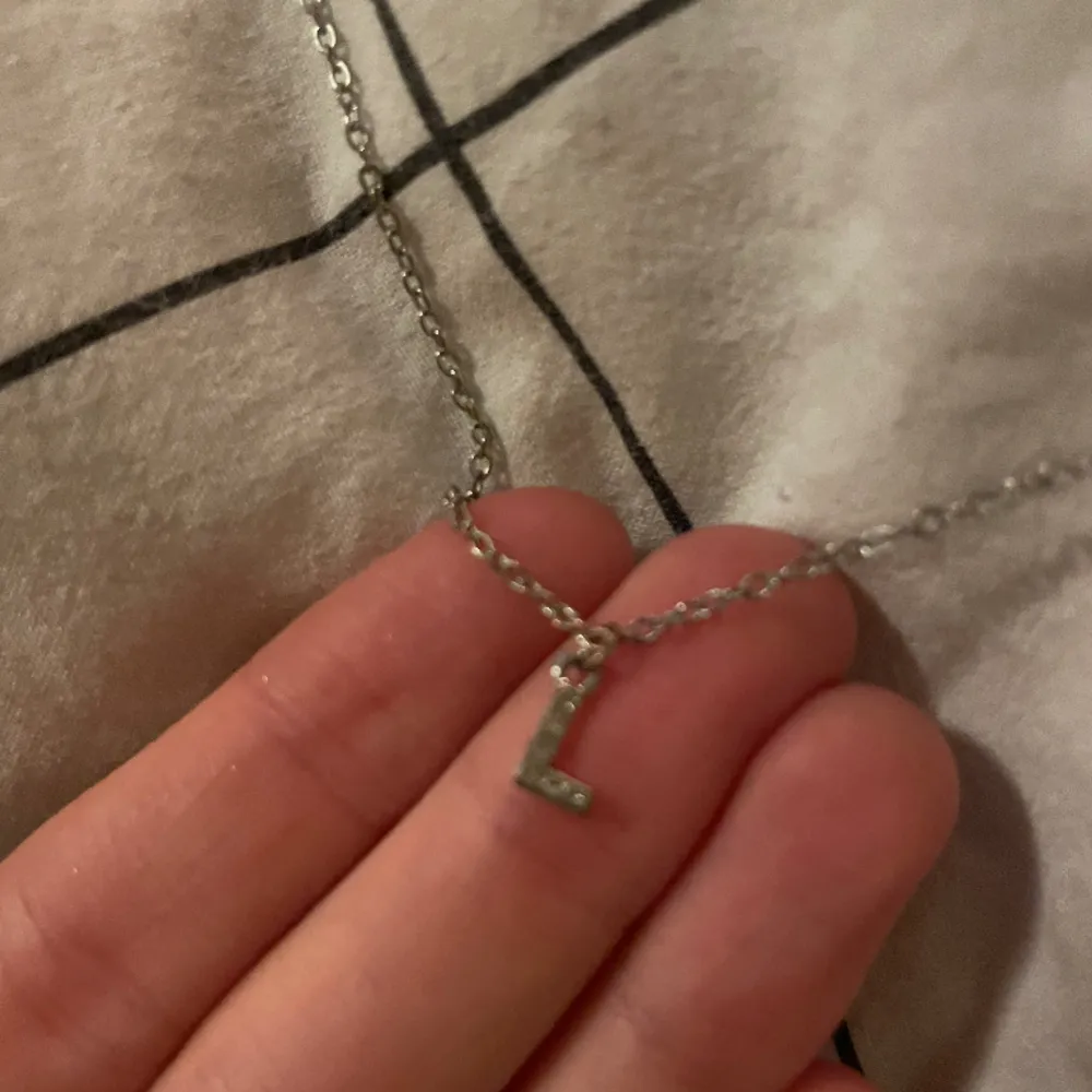 Ett silver halsband med bokstaven L . Asusteet.
