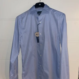 Ljusblå Skjorta - Ljusblå skjorta från Riley. Aldrig använt lappar hänger kvar, helt som ny. Nyskick. Storlek S  Nypris: 700 Mitt pris: 300