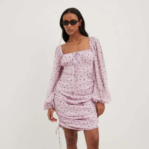 Blommig klänning från NA-KD - Fin klänning från NA-KD, endast använd en gång, säljer då den är en storlek för liten! Klänningen är inte töjbar vid benen 