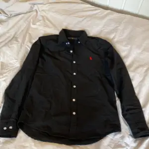  Riktigt snygg svart Ralph Lauren skjorta, perfekt på sommaren nu också med uppkavlade skjortärmar. Den är i mycket bra skicka och allt det bra ut, Mest legat i garderoben så tycker att någon annan kan ha bättte användning av den här fina skjortan. 