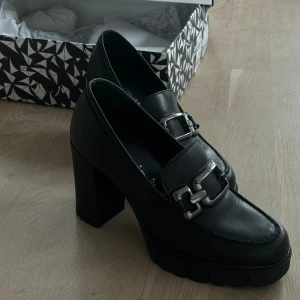 Tamaris Loafer Pumps med platå - Nypris: 1400kr Klackhöjd: 9,5cm Nyskick, använda 1 gång. Loafers med klack i äkta skinn, lika bekväma som snygga. Måste tyvärr säljas då passformen inte blir helt rätt även med inlägg. Nybehandlade med skokräm.  Slutsålda både på Scorett och Håkansso