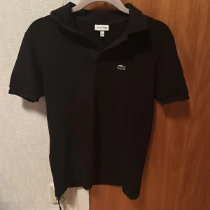 Svart Lacoste pikétröja  - Säljer denna Lacoste pikétröja i storlek 176cm i mycket bra skick och för mycket bra pris! Tröjan har använts knappt tio gånger och är så gott som ny.