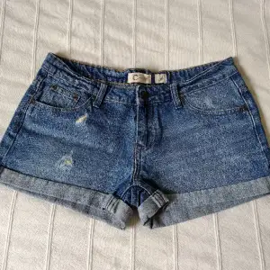 Blå korta jeansshorts från Cubus i 100% bomull. Sparsamt använda och i fint skick. Snygga slitna detaljer och låg midja. Storlek 36.