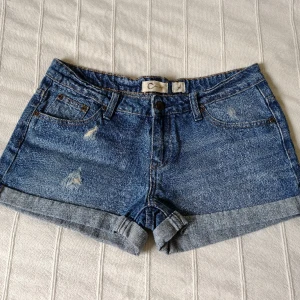 Blå korta y2k jeansshorts i 100% bomull, storlek 36 - Blå korta jeansshorts från Cubus i 100% bomull. Sparsamt använda och i fint skick. Snygga slitna detaljer och låg midja. Storlek 36.