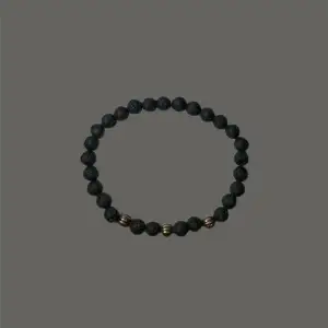 Pärlarmband med svarta lavaliknande pärlor och guld- och kopparfärgade mellandelar. Hefaistos är ett stilrent armband som passar såväl till vardags som till festligare ögonblick. Armbandet har en omkrets på cirka 19 cm. 