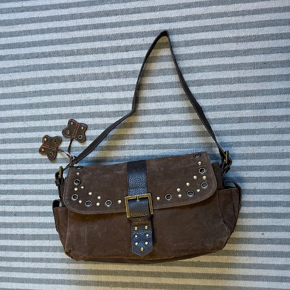 Unik shoulderbag i vegansk brun mocha/läder med magnetknapp. Justerbar axelrem med två små fjärilar, innerfickor och ett litet fack på varje kortsida. Större modell och väldigt rymlig. Sparsamt använd. Väskor.