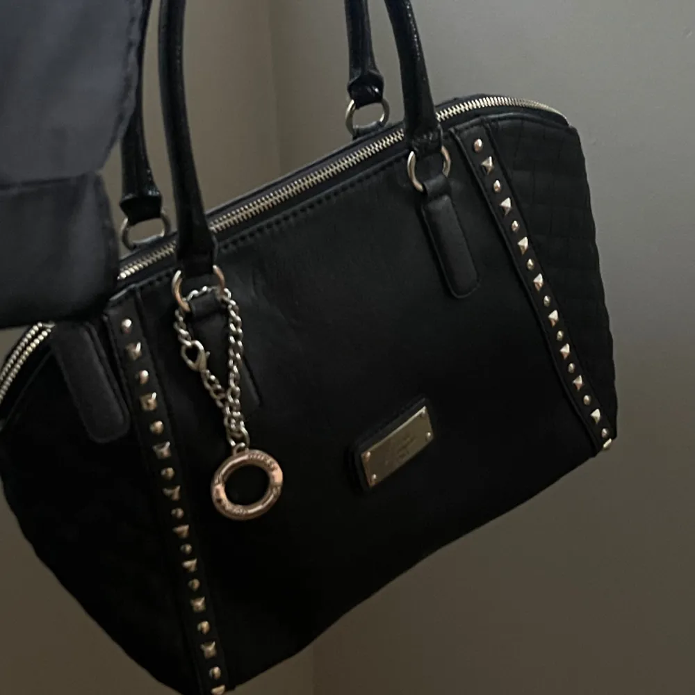 Jättesnygg svart väska från Guess! Köpt på Sellpy därav äkthetskontrollerad💓 Bredd: 30cm, djup: 19cm, höjd: 22cm. Väskan har  defekter. (Skriv för fler bilder). Väskor.
