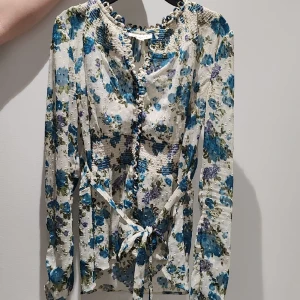 Blommig blus - En vit blus med blåa blommor på. Den har många små delataljer.