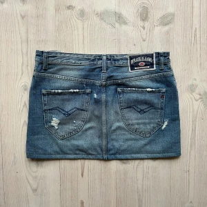 Lågmidjad jeanskjol från Replay - Lågmidjad jeanskjol från Replay som jag har sytt upp från en längre kjol. Fint skick. Står storlek 27 och jag skulle säga att den passar S och M. Tvärs över midjan är det 38 cm längs med sidan är det 33 cm. Använd gärna köp nu!